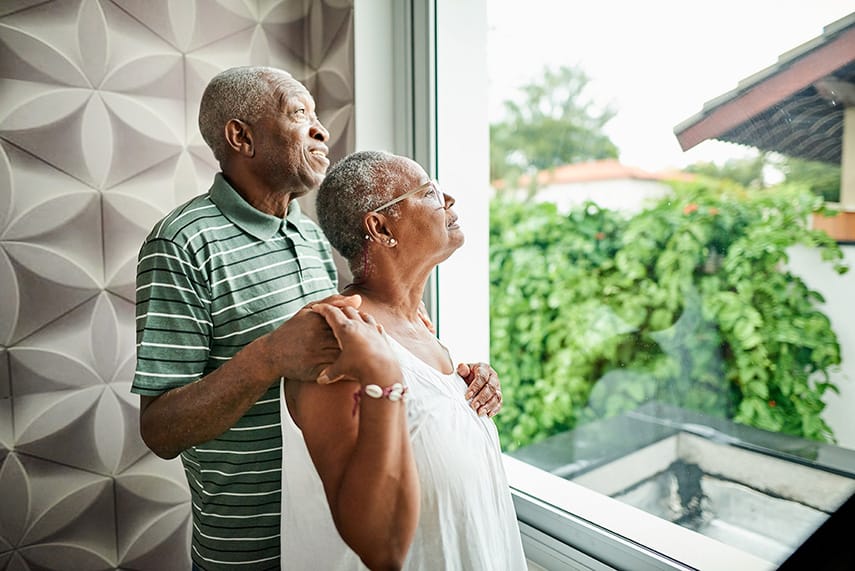 Elderly back couple look out a window of a residence