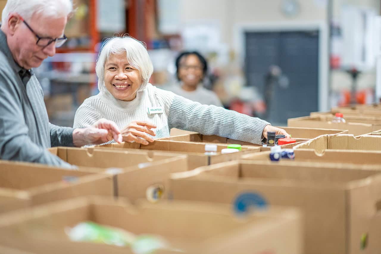 Two elderly people volunteering at a food bank.