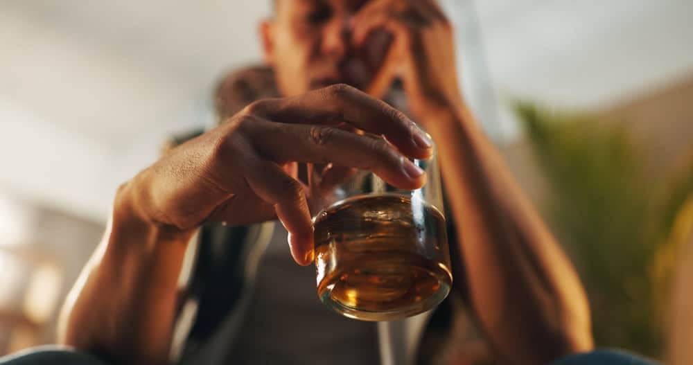 Person holding a glass of alcohol, showing signs of depression and loneliness.