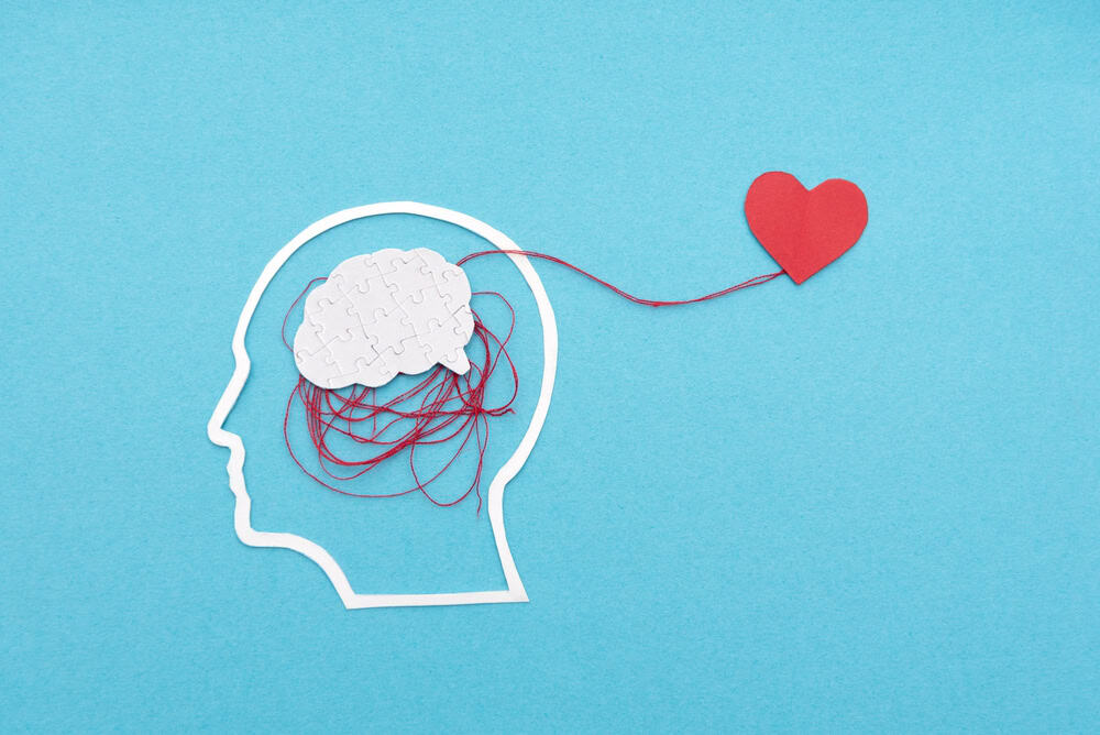 Illustration of a brain and heart connected by a red thread on blue background.