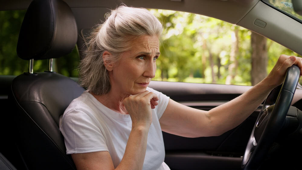 Elderly woman in car showing signs of worry or sadness.