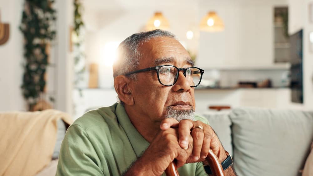 Older man with glasses sitting thoughtfully in a cozy living room.