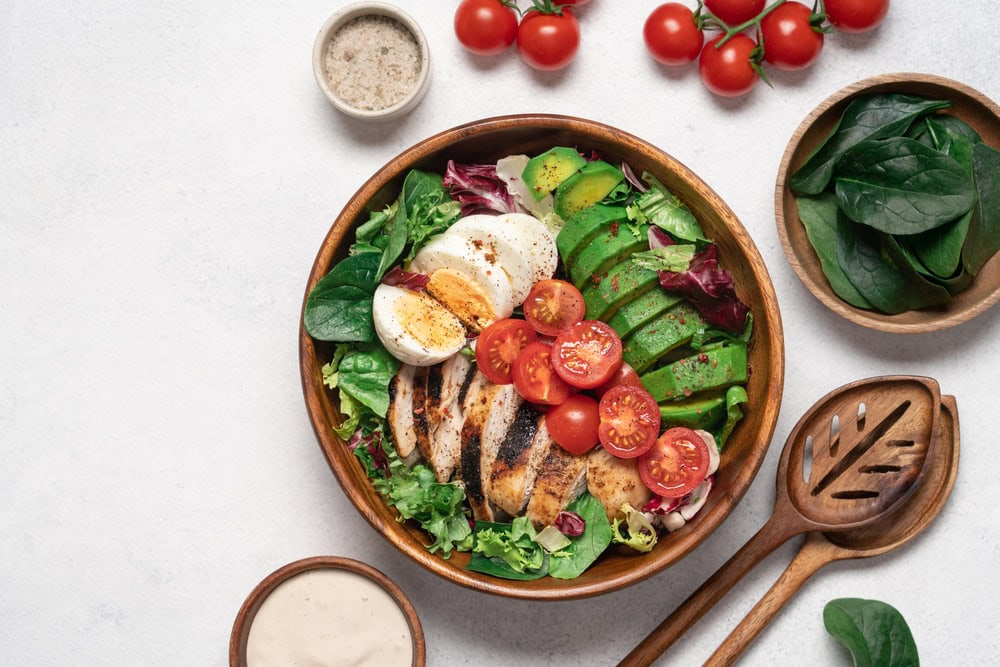 A bowl filled with a nutritious meal. Leafy greens, meat, eggs, tomatoes, avocado